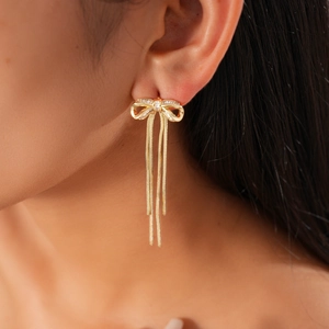 Detail of 18K gold plated bow earrings with zircon and fringe tassels on a model