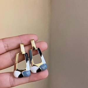 Golden geometric earrings with blue white black enamel mosaic on a minimalist backdrop