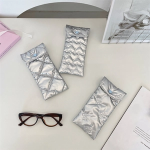 Three silver quilted PU leather glasses pouches with heart and bow patterns on a desk