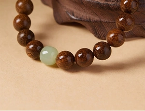 Macro shot of polished brown sandalwood prayer beads featuring a green jade accent bead