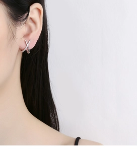 Close-up of elegant silver X-shaped stud earring with diamonds worn on the earlobe