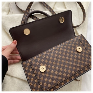 Detail of brown monogram shoulder bag featuring dual gold magnetic snap buttons and PU leather