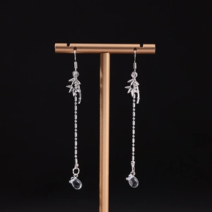 Détail de boucles d'oreilles feuille de bambou argentée avec longues chaînes à pompons
