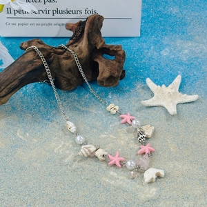 Detail of beaded necklace with pink starfish and white shell charms on beach sand