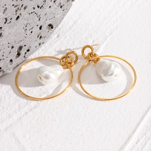 Detailed view of Baroque pearl earrings with layered gold metal rings on a stone surface