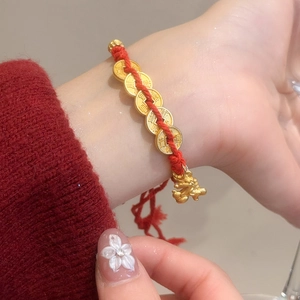 Detailed view of woven red string bracelet with gold coins and Pixiu charm on wrist