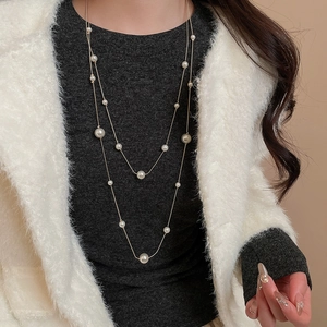 Close-up of elegant double-layered pearl sweater necklace on a grey knit sweater