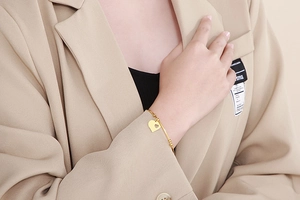 Detail of elegant gold-tone heart charm open bangle worn with a stylish suit sleeve
