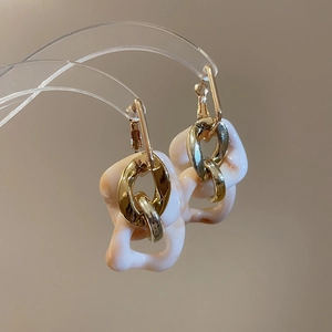 Close-up of dangling earrings featuring gold metal and cream resin geometric links
