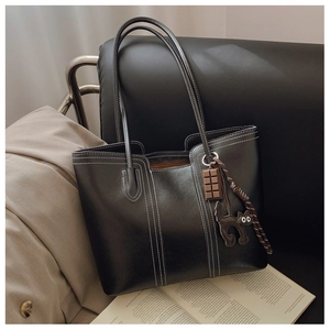 Detail of black leather tote bag with unique cat and chocolate charms on a leather sofa
