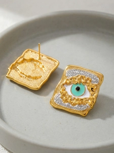 Macro view of gold square stud earrings with evil eye motif and textured metal finish