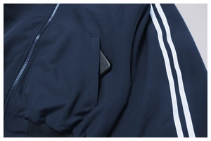 Dettaglio della tasca laterale della giacca sportiva blu navy con strisce bianche e zip