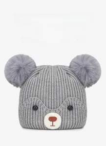 Close-up of winter baby knitted hat with grey faux fur pom-poms and cartoon bear face