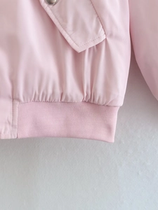 Detail of pink jacket showing ribbed elastic hem and metal snap button pocket flap