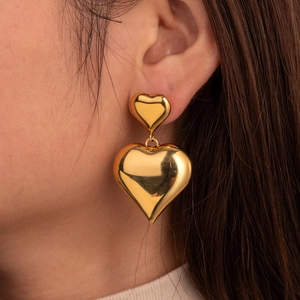 Golden double layer heart-shaped drop earrings in polished stainless steel on a model
