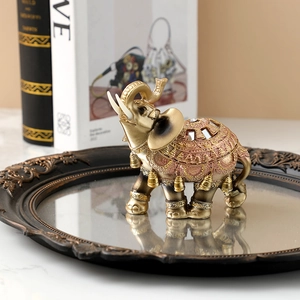 Golden resin elephant figurine with ornate carvings on a round mirrored tray display