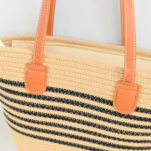 Detail of beige straw tote bag with black stripes and orange leather handles with stitching