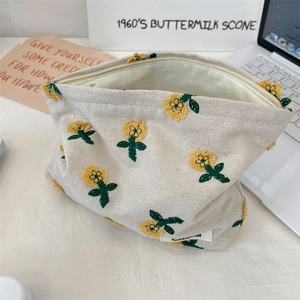 Détail de la broderie florale jaune sur une trousse de maquillage en toile crème zippée