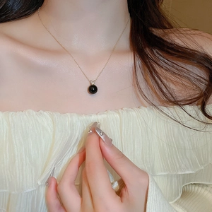 Close-up of minimalist gold necklace featuring a sleek black pearl pendant on a model