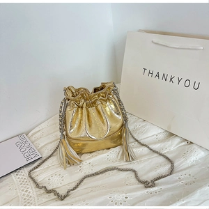 Detail view of gold crocodile embossed bucket bag with drawstring and tassel fringe