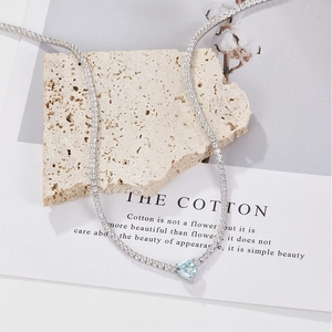 Macro detail of silver heart necklace with light blue zircon on white stone and magazine