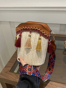 Close-up of bohemian woven straw bucket bag with leather trim and colorful tassel detail