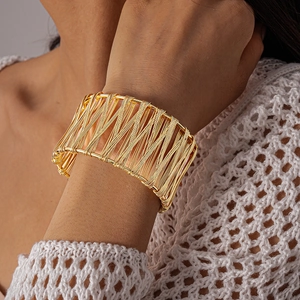 Detailed macro shot of a wide gold metal cuff bracelet with artistic woven hollow texture