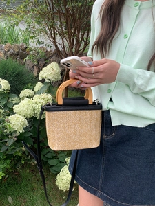 Outdoor shot of a woven straw bucket bag with black leather trim and wooden handle