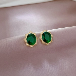 Elegant gold earrings with oval emerald stones and white zircon trim on purple silk