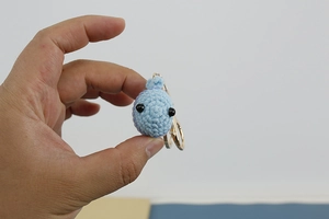 Close-up of a light blue handmade crochet whale keychain with golden metal ring