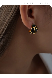 Close-up of elegant gold and black enamel earrings with geometric lines on model