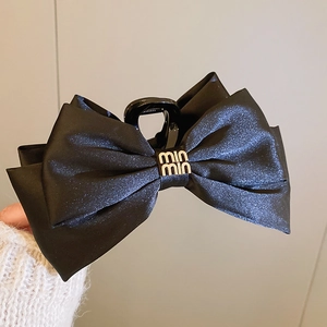Gros plan d'une pince à cheveux en satin noir avec nœud et logo doré élégant