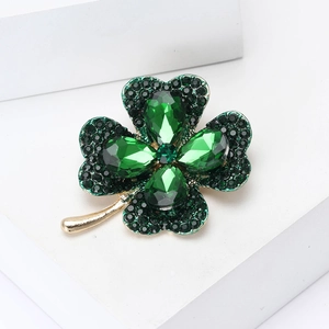 Macro detail of gold-plated clover brooch with vibrant green crystals and rhinestones