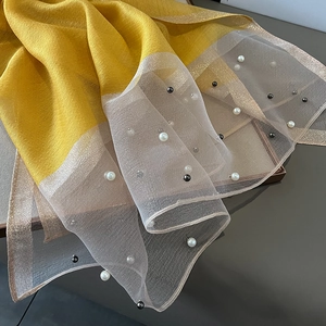 Detail of yellow silk scarf featuring sheer metallic mesh edges and elegant pearl bead accents