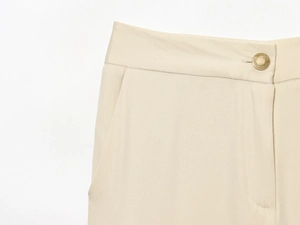 Détail d'un pantalon large beige avec tissu texturé et un bouton cylindrique doré
