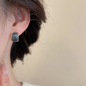 Detail of square gold rimmed earrings with dark stone inlay worn on a model's ear