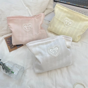 Macro shot of knitted makeup bags with heart lace trim and bow details on bed