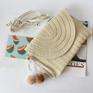 Straw envelope clutch bag with pom pom charms and crossbody strap on white background
