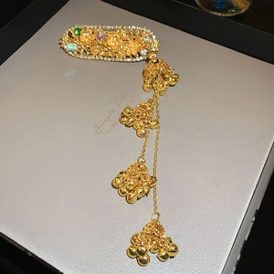 Detail of ethnic gold hair clip with green gemstone, rhinestones and tinkling bell tassels