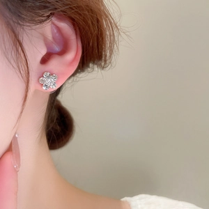 Close-up of sparkling floral silver stud earrings with crystals on a model's ear