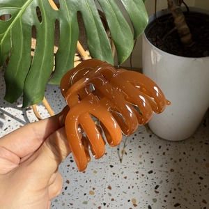 Detail of a glossy amber brown resin shark hair claw clip held in hand with shiny finish