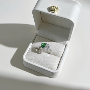 Macro shot of silver ring with pear-cut green and emerald-cut clear stones in a gift box