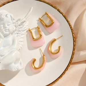 Close-up of pink acrylic C-shaped earrings with gold frames on a white ceramic plate