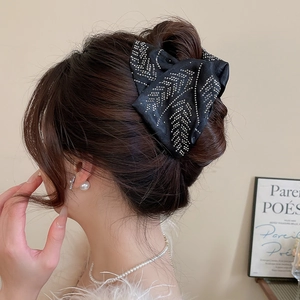 Detail showing an elegant black satin bow hair claw clip with rhinestones worn on hair