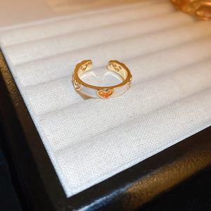 Macro shot of gold heart ring with white enamel and orange cubic zirconia on a jewelry tray
