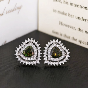 Macro shot of heart-shaped green zircon earrings with white crystal halo on dark background