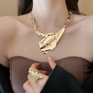 Detailed view of irregular pleated gold necklace and matching ring set on a model