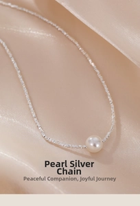 Macro view of a single white pearl on a textured silver chain over champagne silk