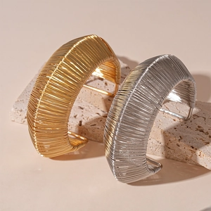 Modern woven metal open cuff bracelets in gold and silver finish on stone display