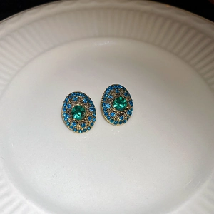 Detail of vintage emerald earrings with blue pavé stones on a white ceramic plate